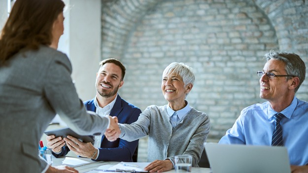 Happy member of human resource team shaking hands with female candidate on job interview in the office.