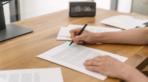 Businesswoman is focused on reviewing paper contracts and documents while taking notes with a pen. Person signing agreement in office